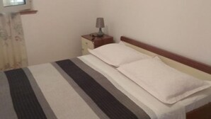 A single bed with a striped bedspread, a bedside table with a lamp, and a window with curtains. - Seafront Charming Apartments Kosirina One Bedroom (Brna)