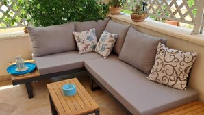 Ein modulares Sofa mit floralen Kissen, ein kleiner Holztisch und Kübelpflanzen auf einem Balkon.