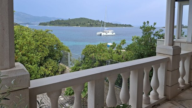 A balcony with a view of a calm sea, a sailboat, and a distant island. - Apartment Jadranka - Two Bedroom Apartment With Balcony And Sea View (Korcula)