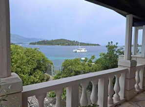 A balcony with a view of a calm sea, a sailboat, and a distant island.