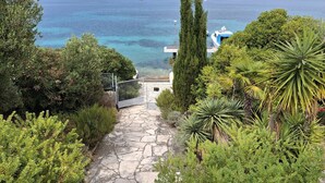 A stone pathway leading to a coastal area with clear blue water, boats, and lush greenery. - Apartment Jadranka - Two Bedroom Apartment With Balcony And Sea View (Korcula)