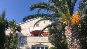 A building with a balcony, palm trees, and a pool with inflatable toys. - Apartment Jadranka - Two Bedroom Apartment With Balcony And Sea View (Korcula)