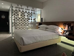 A modern hotel room with a large bed, a bedside table with a lamp, and a glass partition with a unique pattern. - Marvelous 5-bedroom house in Seattle (Seattle)