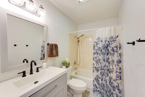 Ein Badezimmer mit einem weißen Waschbecken, einem schwarzen Wasserhahn, einem großen Spiegel, einer Toilette, einer Badewanne und einem Duschvorhang mit Blumenmuster.