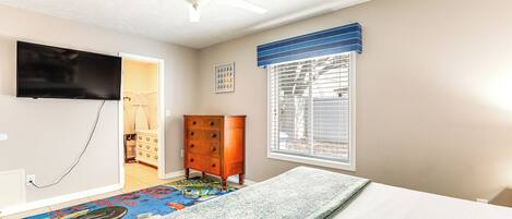 Een slaapkamer met een bed, een plafondventilator, een tv aan de muur, een dressoir en een raam met jaloezieën.