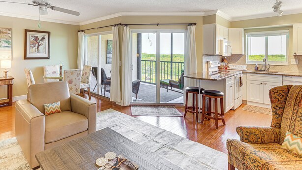 A spacious living area with a sofa, armchair, and coffee table, a kitchen with a view, and a balcony with a sliding door. - 1/2 Mi to Jupiter Beach: Penthouse Condo w/ Views (Jupiter)