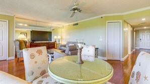 A living room with a round glass table, patterned chairs, a ceiling fan, and a television in the background. - 1/2 Mi to Jupiter Beach: Penthouse Condo w/ Views (Jupiter)