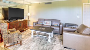 A living room with a sofa, armchair, coffee table, and a TV on a stand. - 1/2 Mi to Jupiter Beach: Penthouse Condo w/ Views (Jupiter)