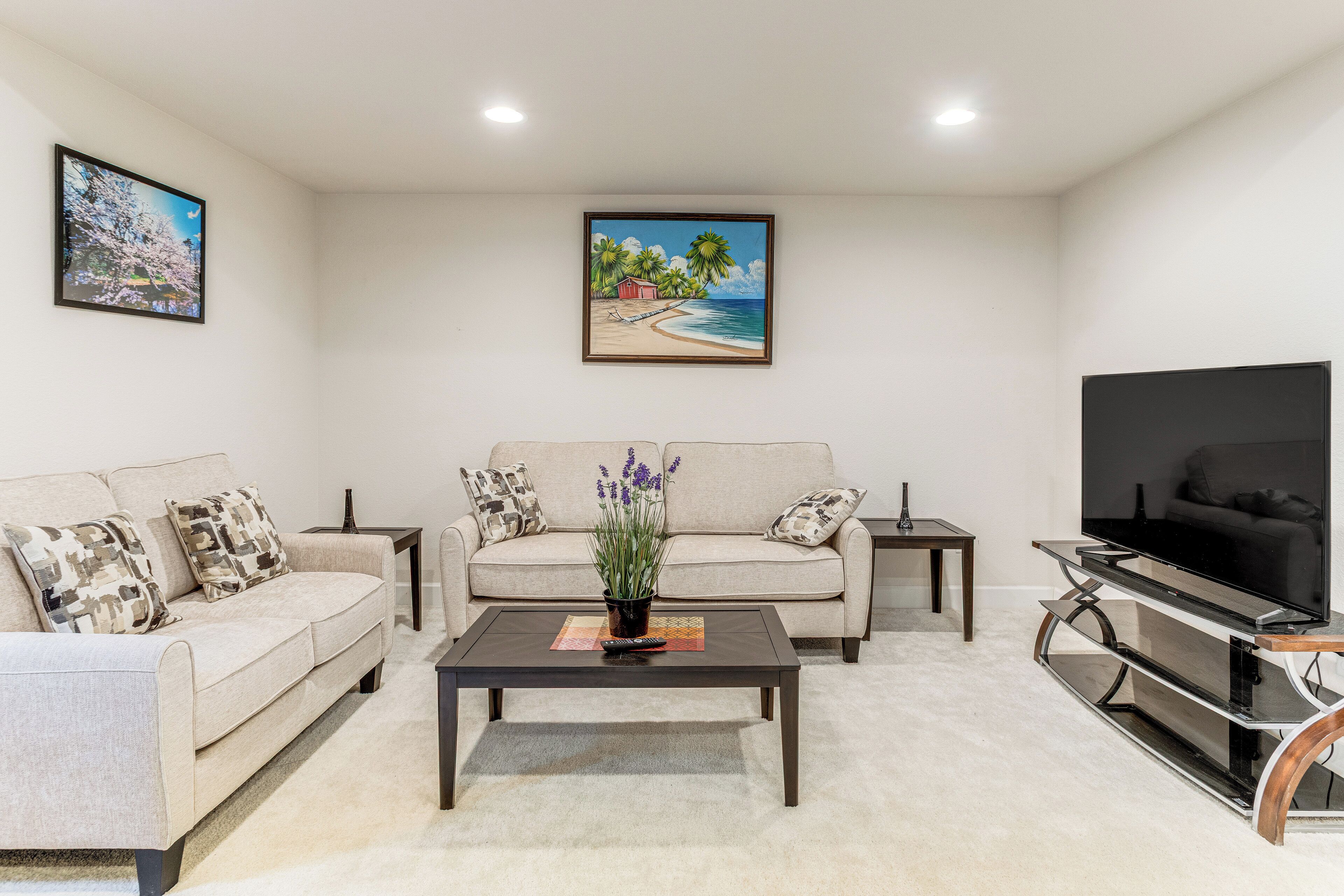 A living room with a beige sofa, a coffee table, a TV stand, and a painting of a beach scene.
