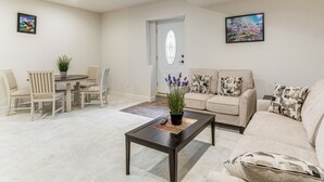 A living room with a beige sofa, a coffee table, and a dining area with chairs and a table. - 12 Mi to Hospitals: Modern Apartment in Aurora! (Aurora)