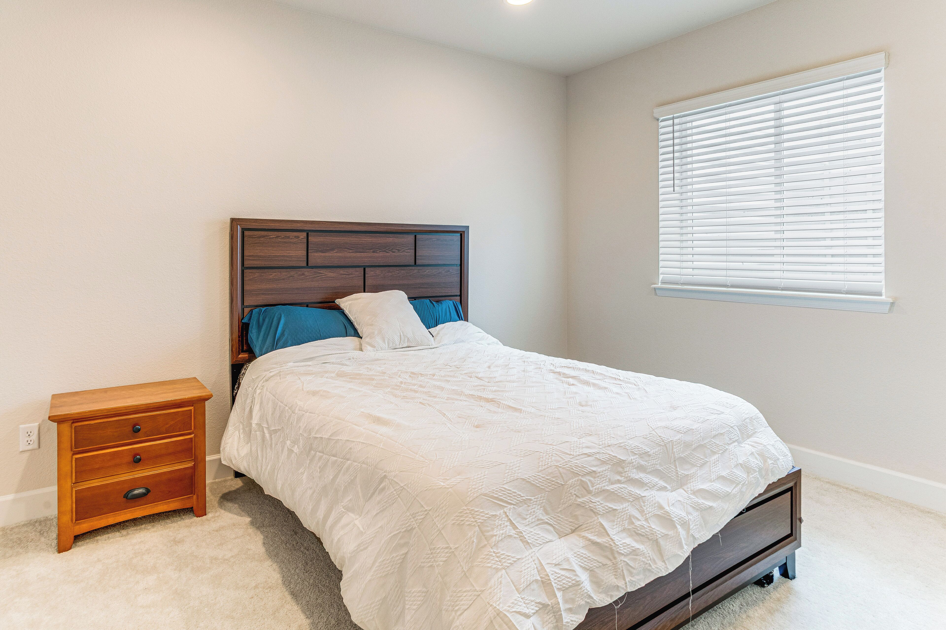 A bedroom with a bed, a nightstand, and a window with blinds.