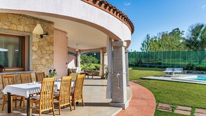 A covered outdoor dining area with a stone wall, wooden chairs, and a table. - Villa 'Iris' with Private Pool, Wi-Fi and Air Conditioning (Costa Rei)
