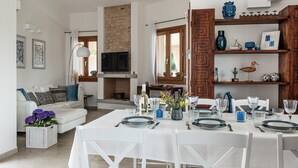 A dining area with a table set for four, a fireplace, and a television in the background. - Villa 'Iris' with Private Pool, Wi-Fi and Air Conditioning (Costa Rei)