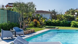 A swimming pool with lounge chairs, a stone wall, and a garden with various plants and a house in the background. - Villa 'Iris' with Private Pool, Wi-Fi and Air Conditioning (Costa Rei)
