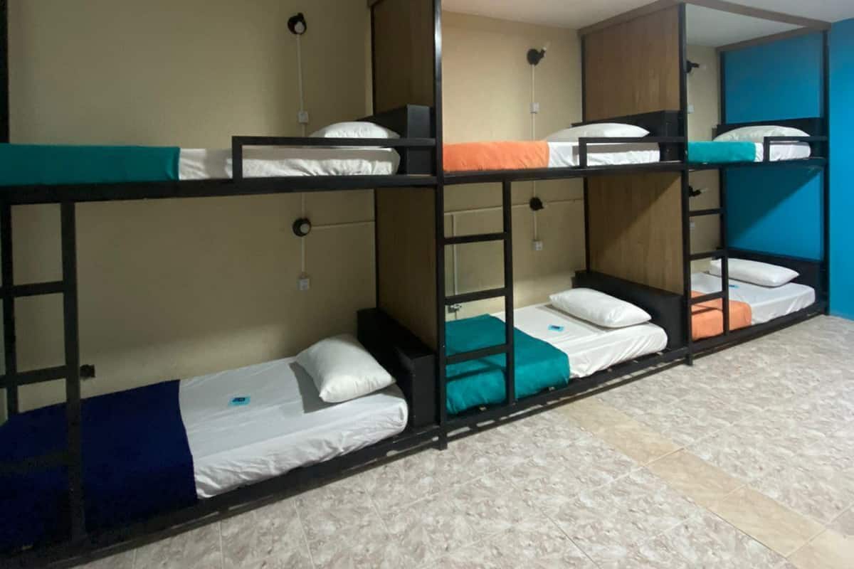 A dormitory room with bunk beds, a tiled floor, and a ceiling light.