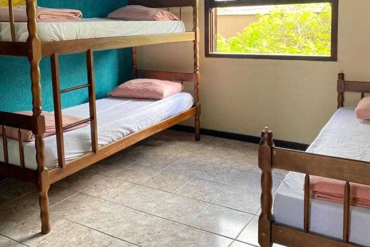 A dormitory room with bunk beds, a window with a view of greenery, and a tiled floor.
