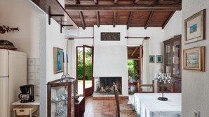 Una habitació acollidora amb una llar de foc, bigues de fusta, una taula de menjador i un armari amb vidrieres.
