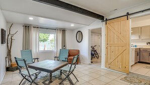 Un coin repas avec une table et des chaises en bois, un tapis à motifs et une vue sur la cuisine par une porte ouverte.