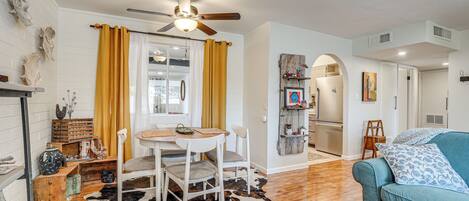 A living room with a wooden floor, a cowhide rug, a teal sofa, a dining table with chairs, and a ceiling fan.