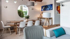 Uma sala de jantar com uma mesa de madeira, cadeiras brancas, um espelho redondo e uma planta em vaso.