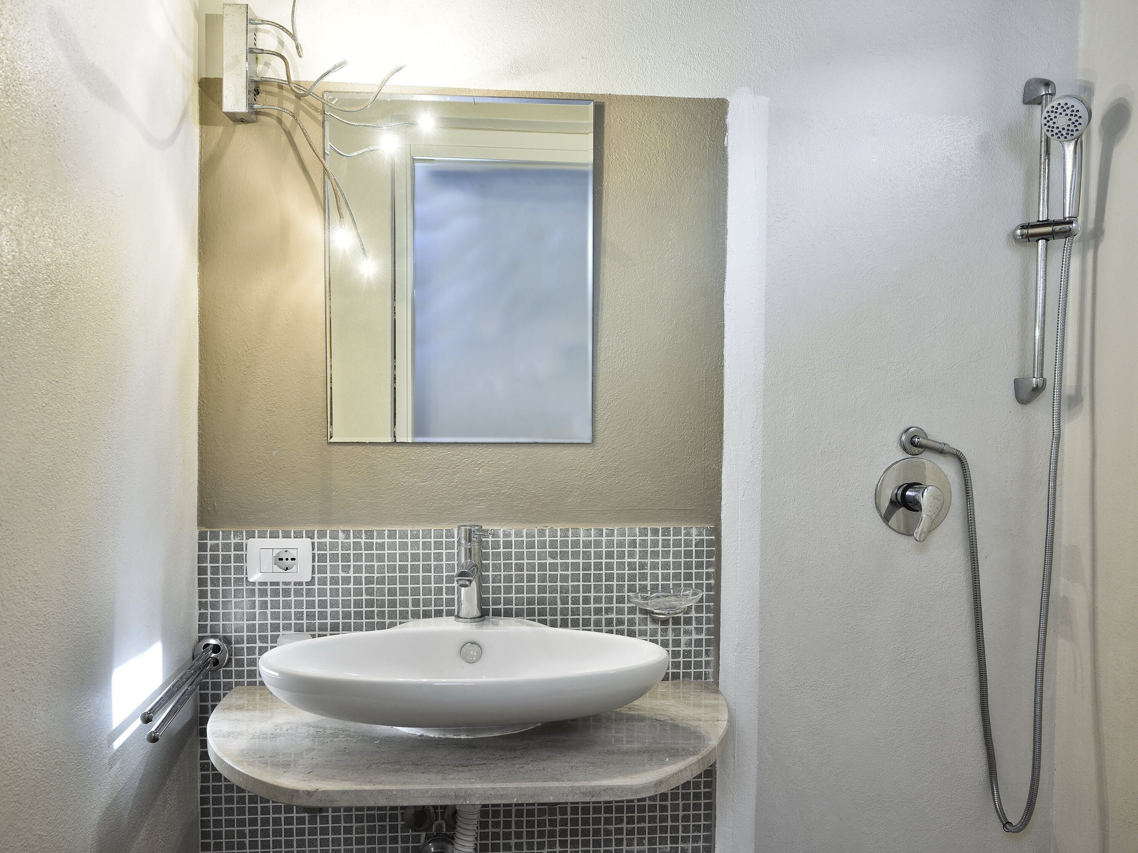 Ein Badezimmer mit weißem Waschbecken, einem Spiegel, einer Dusche und einer gefliesten Rückwand.