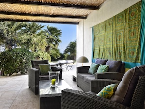 An outdoor seating area with wicker furniture, a glass table, and a patterned wall. - Villa 'Quattro' with Sea View, Wi-Fi and Air Conditioning (Costa Rei)