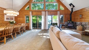 L’intérieur chaleureux d’un chalet comprend un coin repas, un salon avec un canapé, une cheminée et de grandes fenêtres offrant une vue sur l’extérieur.