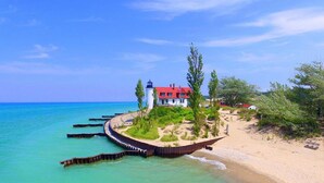 Une propriété située sur la côte, comprenant un phare, une maison au toit rouge et une plage de sable.