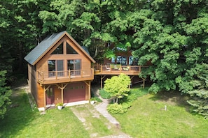 A wooden cabin with a balcony and a deck, surrounded by dense trees.