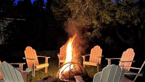 Una fogata con cuatro sillas Adirondack dispuestas a su alrededor en un entorno al aire libre.