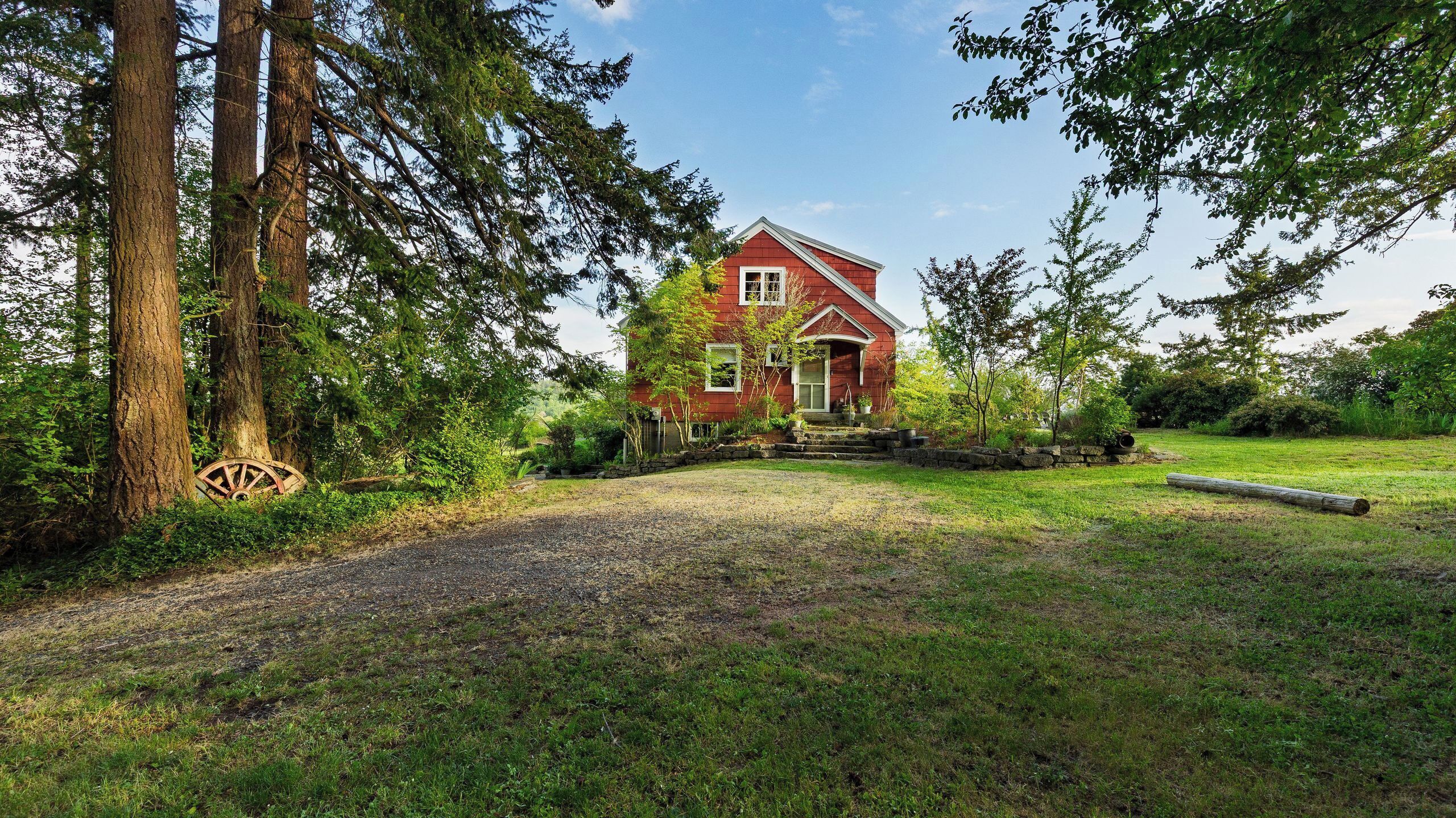 A red house with a stone pathway leading to the entrance, surrounded by trees and greenery.