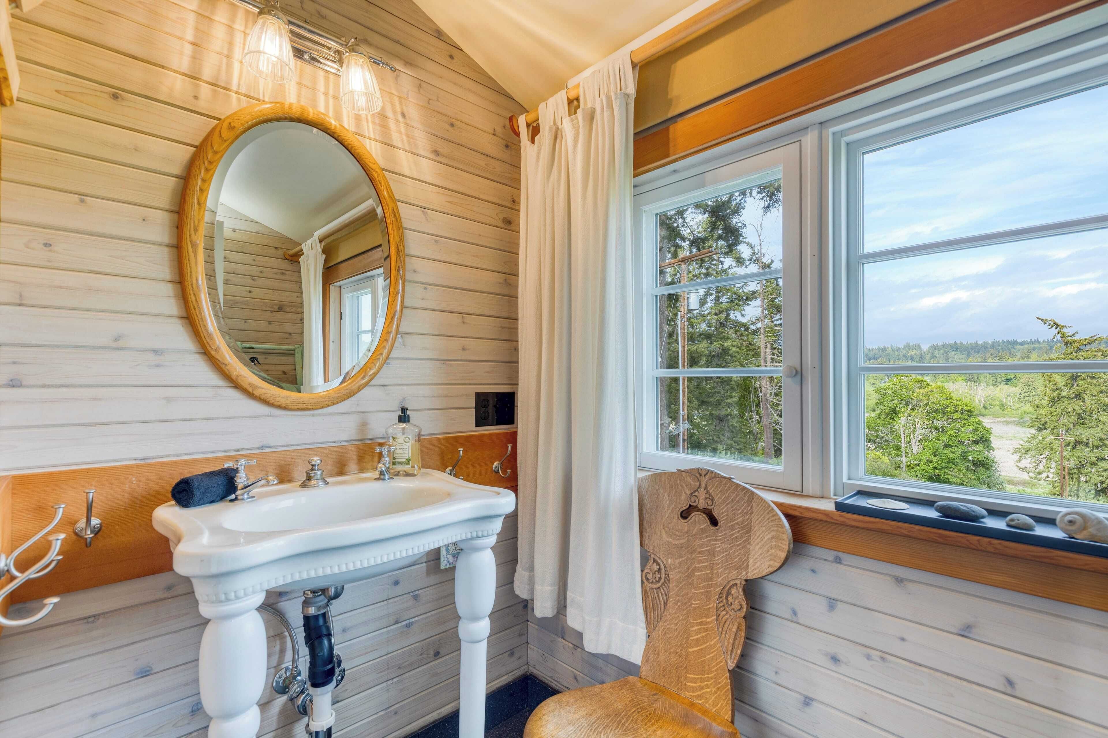 A bathroom with a wooden interior, a white sink with a mirror, and a window with a view of trees.