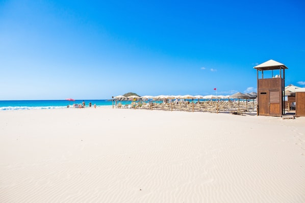 A beach with a wooden structure, umbrellas, and beach chairs.