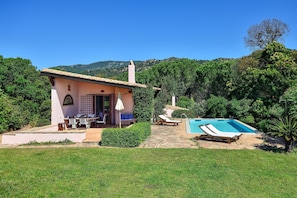 A house with a pool, patio furniture, and a view of the surrounding greenery.