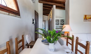 A narrow hallway with a wooden table, chairs, a vase with flowers, and a lamp.