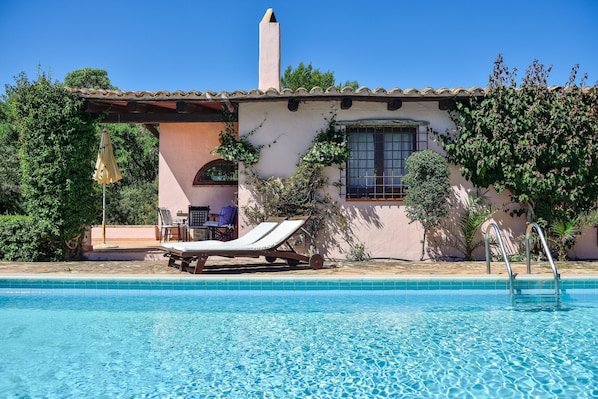 A swimming pool with lounge chairs, a patio area, and a building with a tiled roof and window. - Villa 'Fiori 3' with Sea View, Wi-Fi, and Air Conditioning (S.Margh.di Pula)