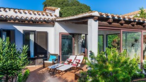 A house with a tiled roof, a covered patio with two lounge chairs, and a glass door leading to a garden. - Villa '12' with Private Terrace, Wi-Fi and Air Conditioning (Costa Rei)