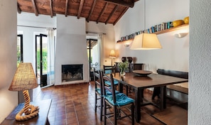 A cozy room with a fireplace, a dining table, chairs, a lamp, and a bookshelf.