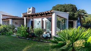 A modern house with a glass conservatory, a garden with various plants, and a clear blue sky. - Villa '12' with Private Terrace, Wi-Fi and Air Conditioning (Costa Rei)