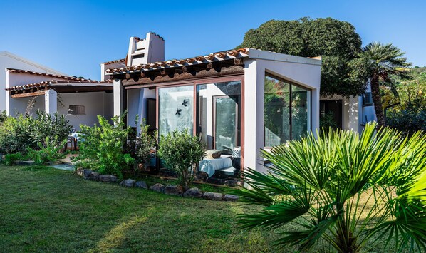 A modern house with a glass conservatory, a garden with various plants, and a clear blue sky.