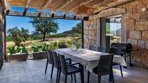 An outdoor patio with a stone wall, a table with chairs, a grill, and a view of the countryside. - Villa 'Laccus 6' with Sea View, Wi-Fi and Air Conditioning (Castiadas)
