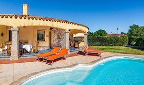 Un área junto a la piscina con sillones de descanso, un pilar de piedra y vistas a la piscina.