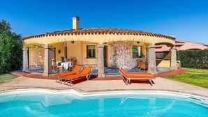 Un área junto a la piscina con sillones de descanso, una mesa de comedor y un muro de piedra.