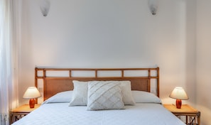 Una cama con cabecera de madera, dos lámparas de noche y una colcha blanca con textura.