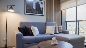 Un salon moderne avec un canapé gris, une table basse ronde et un tableau représentant un paysage urbain, encadré et accroché au mur.