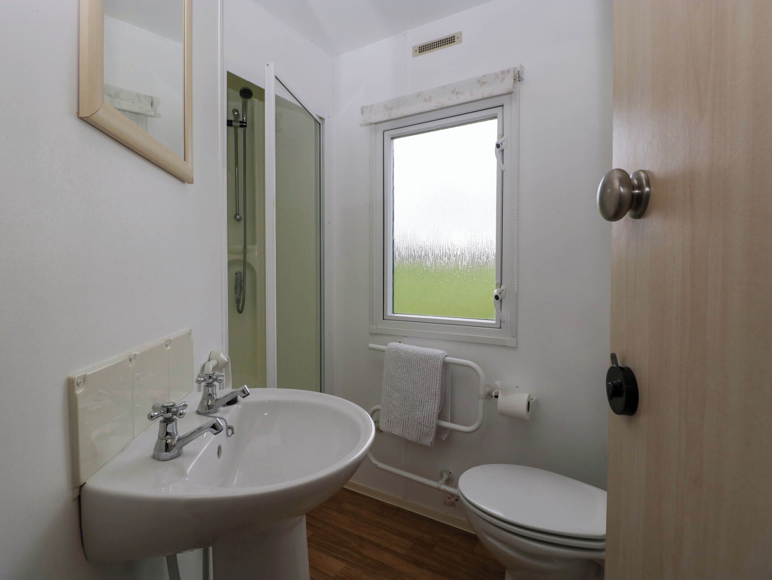 Un baño con lavamanos, inodoro y ventana con vista a un campo.