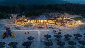 Ein Strandhotel mit einem zentralen Gebäude, Außenbereich mit Sitzgelegenheiten und Sonnenschirmen.