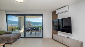 A modern living room with a large TV, a sofa, and a balcony with a view of the city and hills. - Apartment SEASIDE II with panoramic seaview (Polje)