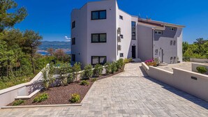 A modern two-story building with a flat roof, large windows, and a paved driveway leading to the entrance. - Apartment SEASIDE II with panoramic seaview (Polje)