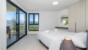 A modern bedroom with a large sliding glass door leading to a balcony, a bed with neatly folded towels, a round mirror, and a bedside table with a lamp. - Apartment SEASIDE II with panoramic seaview (Polje)
